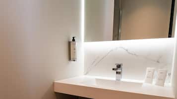 Un baño moderno con encimera de mármol blanco, lavabo integrado, espejo y cubo de basura.