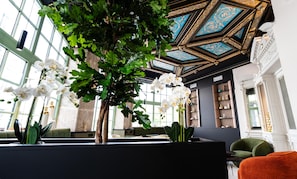 Interior moderno com uma grande árvore, estantes de livros e um design geométrico no teto.