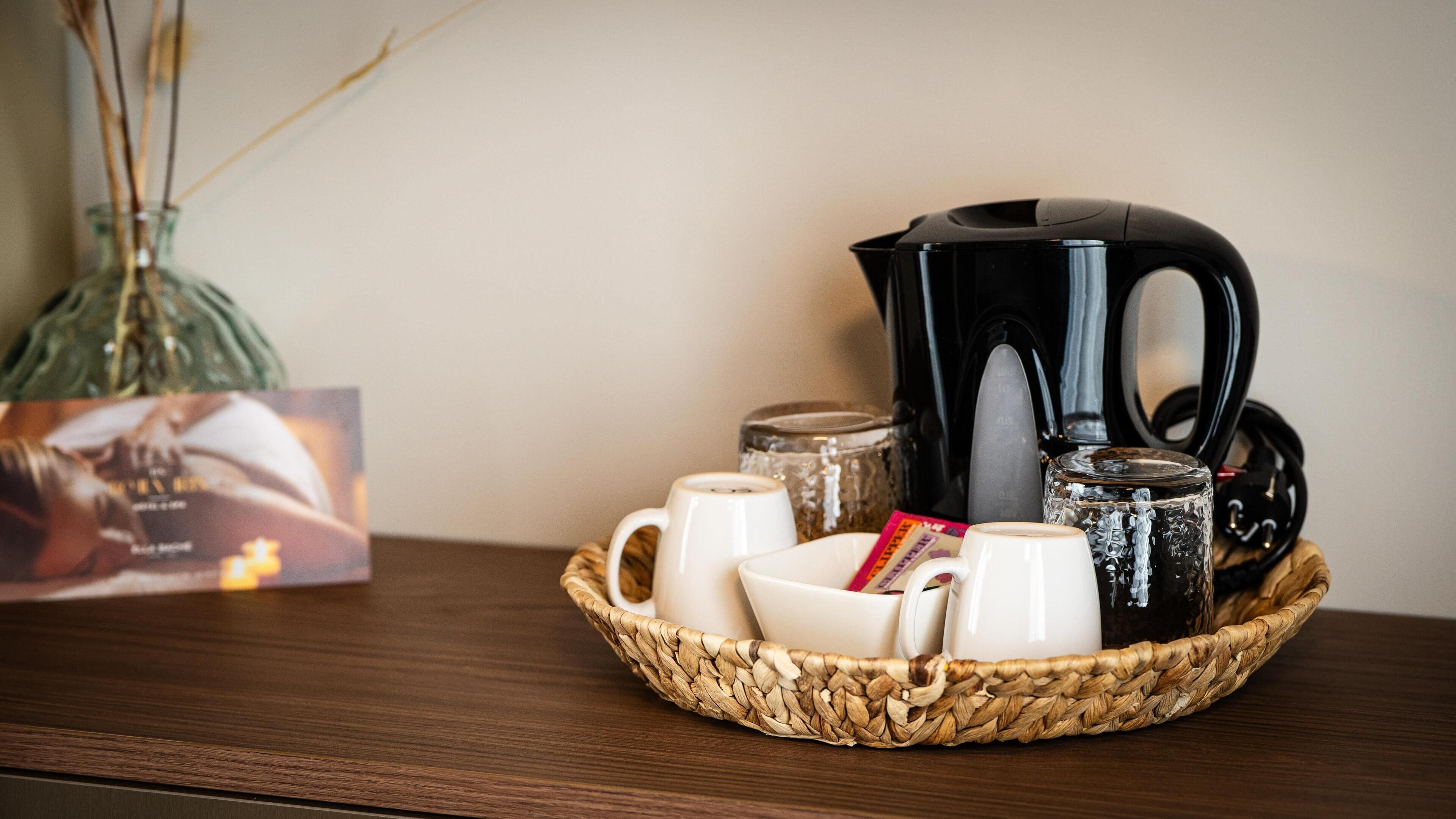 A coffee setup with a black coffee pot, white cups, and a woven basket on a wooden table.