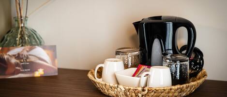 A coffee setup with a black coffee pot, white cups, and a woven basket on a wooden table.