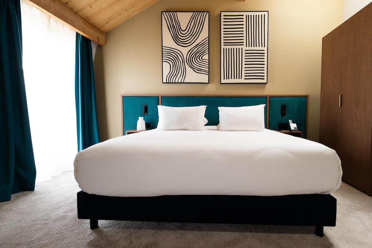 Una cama grande con cabecera de madera, dos mesitas de noche con lámparas y arte abstracto en la pared.