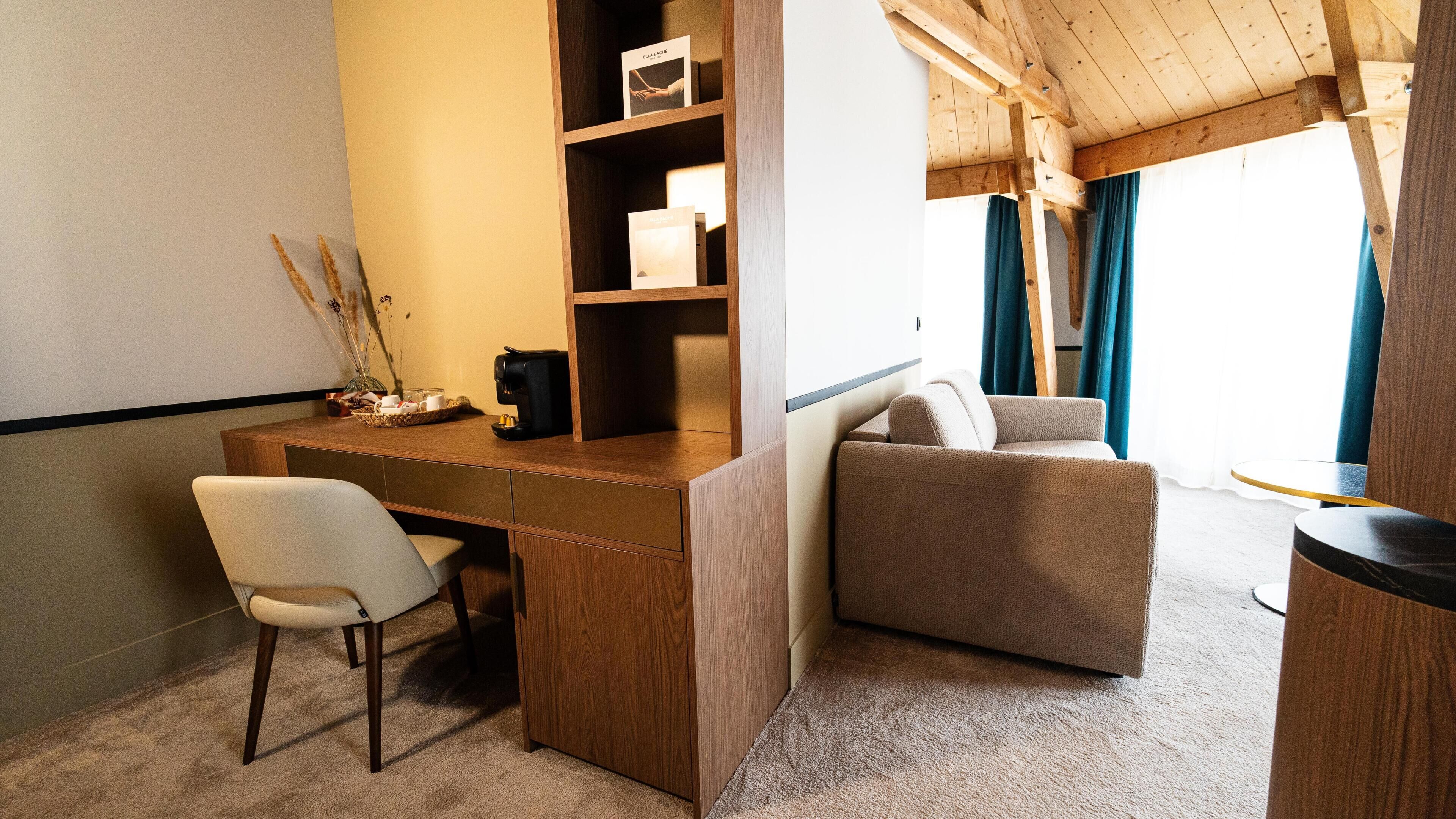 A cozy room with a wooden desk, a comfortable armchair, a coffee maker, and a bookshelf.