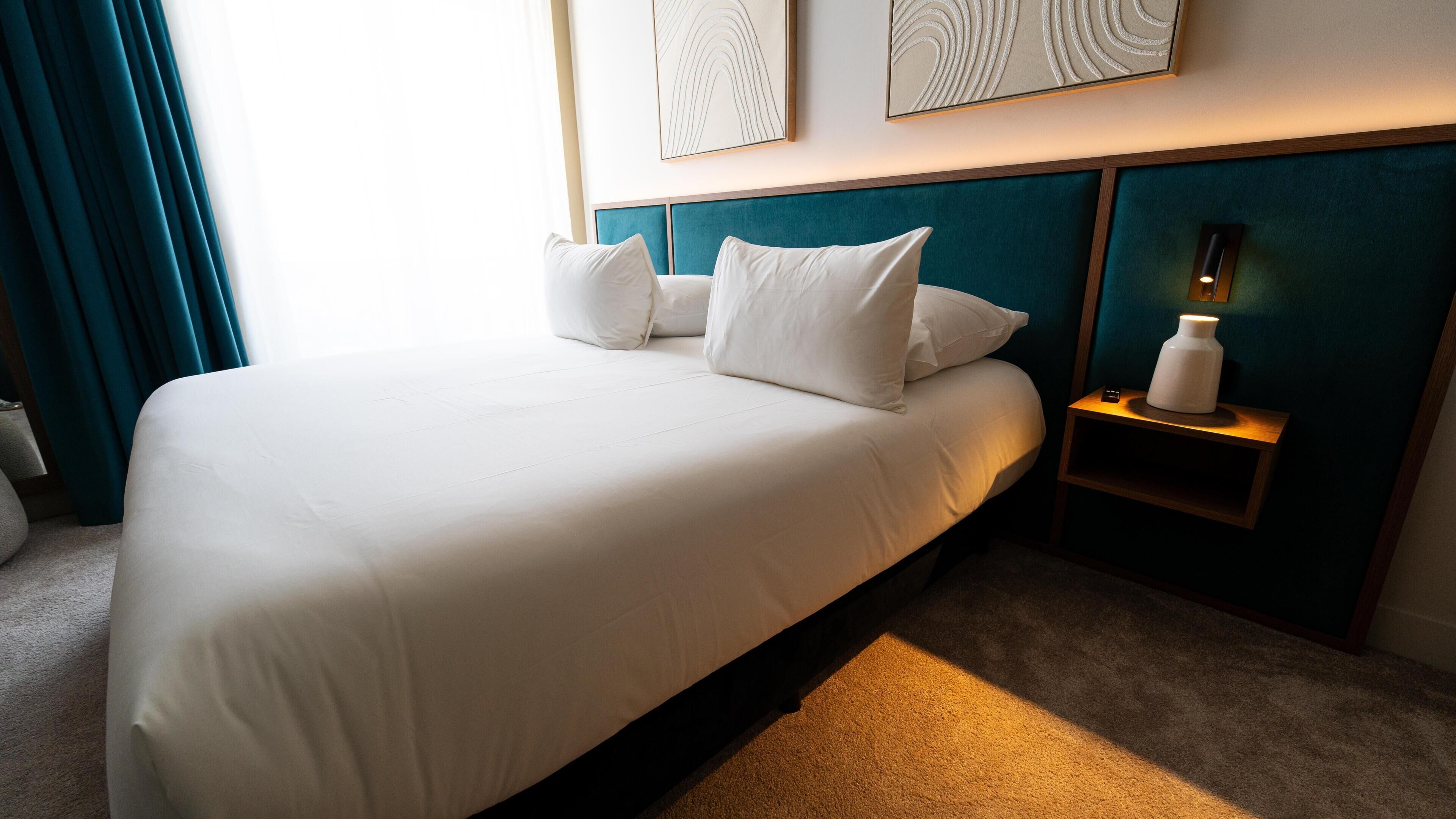 Una habitación de hotel con una cama grande, una mesita de noche con lámpara y una obra de arte en la pared.