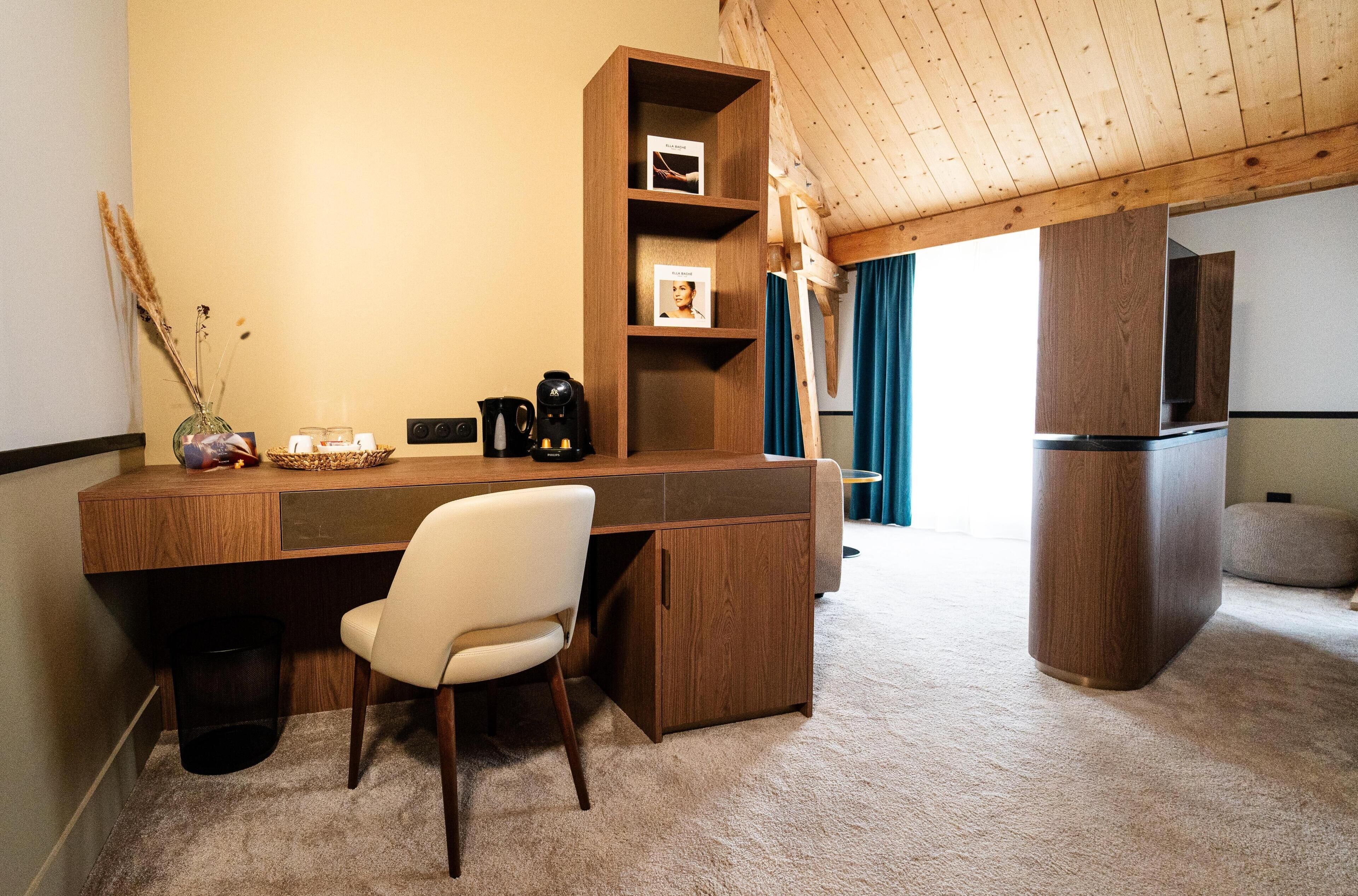 Una habitación pequeña con un escritorio de madera, una silla, una estantería, una cafetera y un refrigerador.