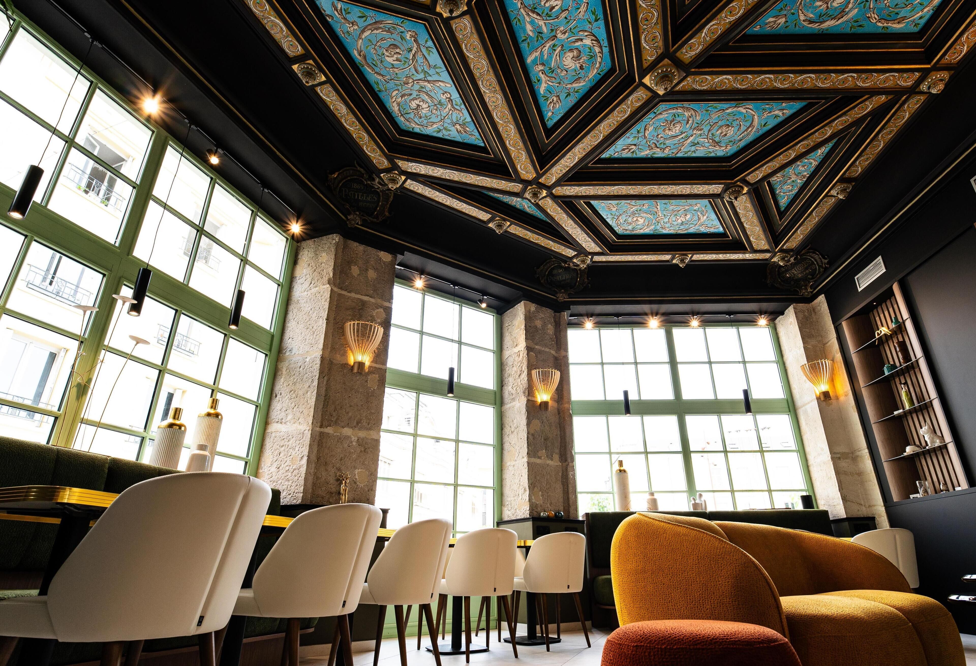 A room with a high ceiling, large windows, and a seating area with chairs and a sofa.