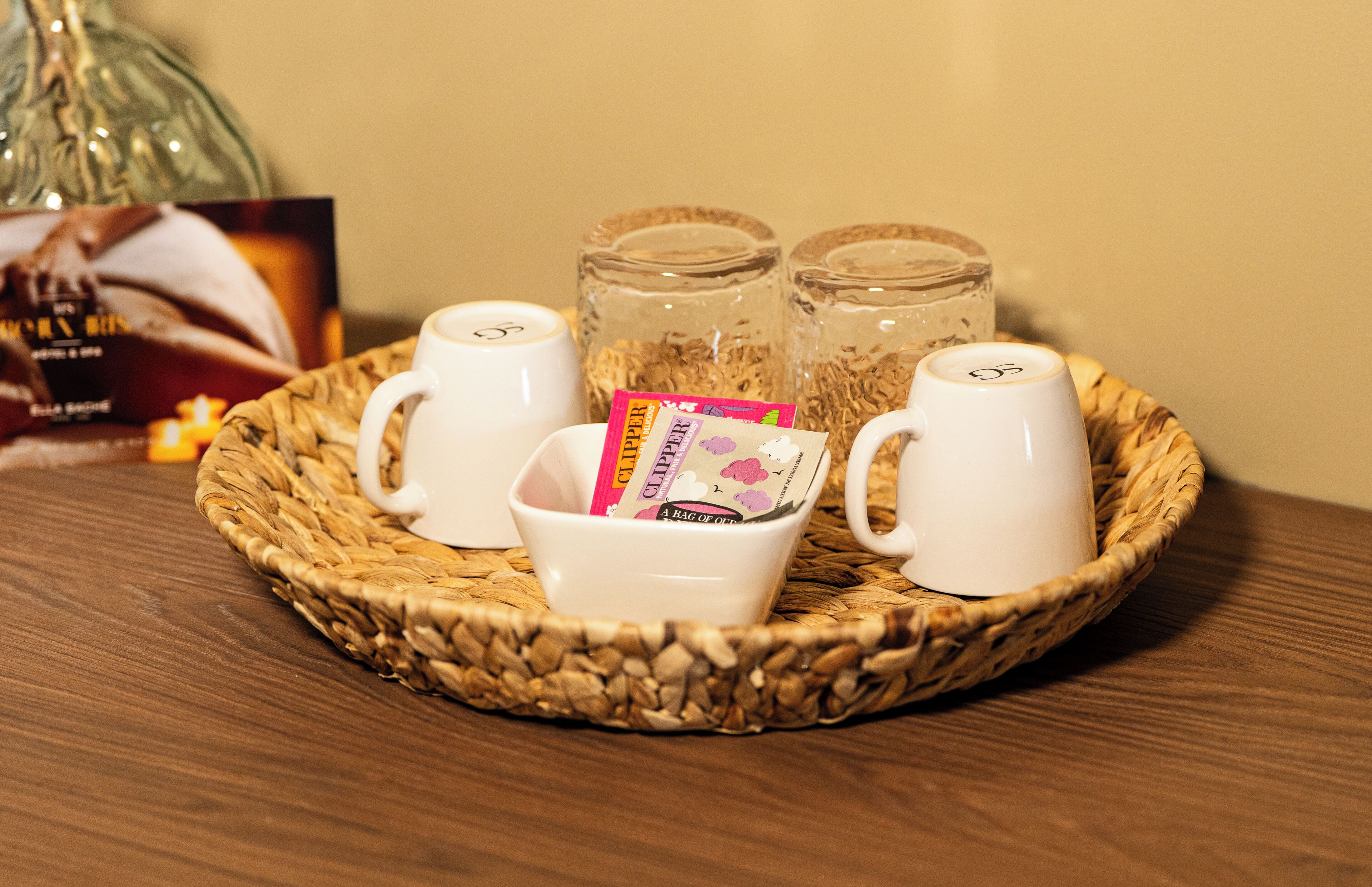 A tray with two white cups, a small bowl with tea bags, and two glass jars on a wooden table.