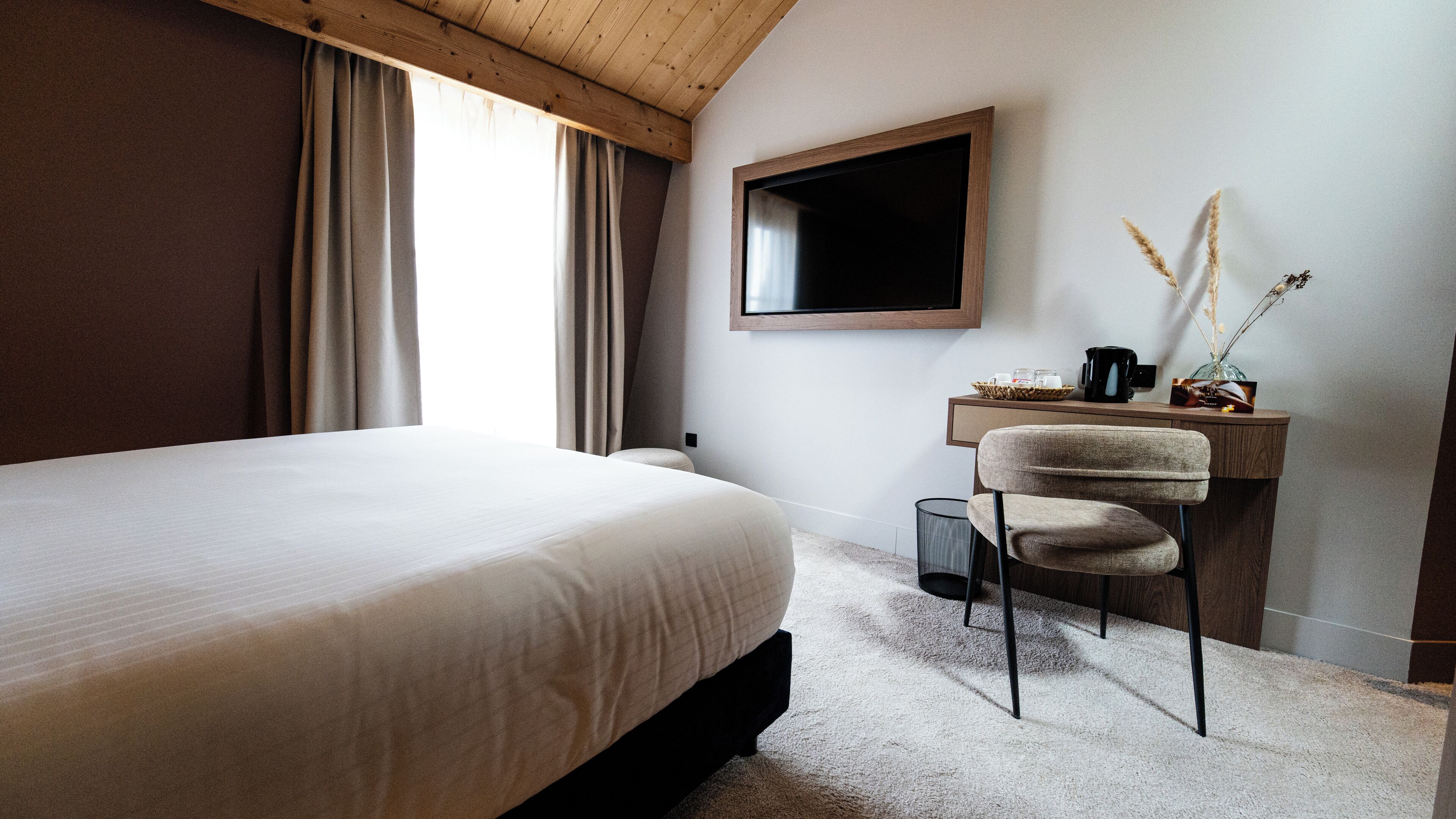 Un dormitorio con cama, escritorio, silla, espejo y ventana con cortinas.