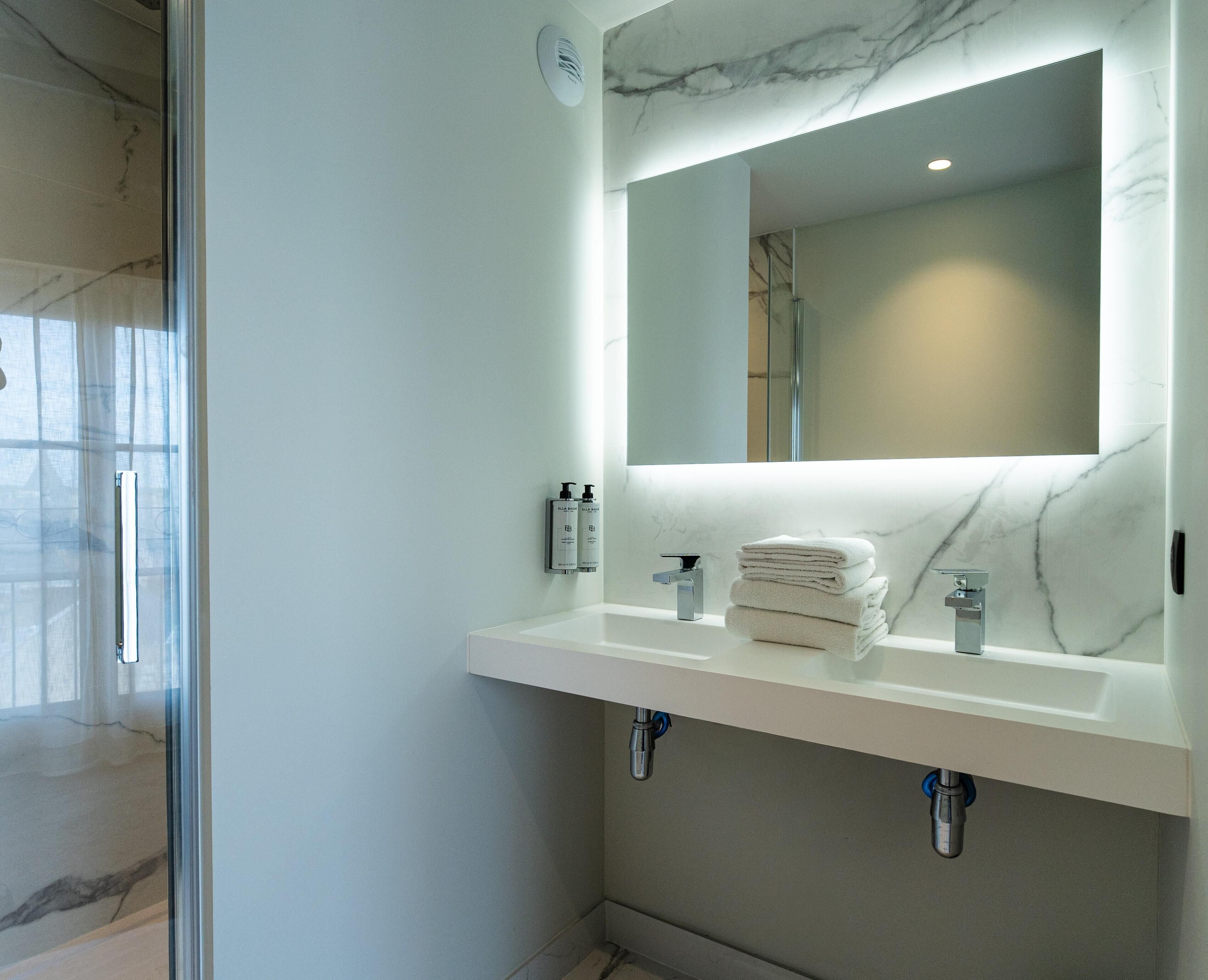 A modern bathroom with a marble countertop, a large mirror, and a stack of white towels.