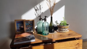 Una mesa de madera con un libro, dos botellas de vidrio, un jarrón con plantas secas y un cuenco decorativo.