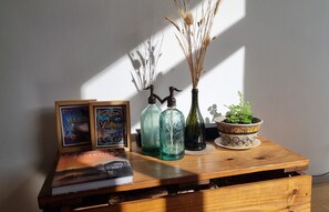 Una mesa de madera con un libro, dos botellas de vidrio, un jarrón con plantas secas y un cuenco decorativo.