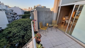 Un balcón con una mesa y sillas, una planta en maceta y vistas de la ciudad.