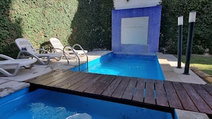 Una piscina con muelle de madera, sillas de descanso y pared de azulejos azules.