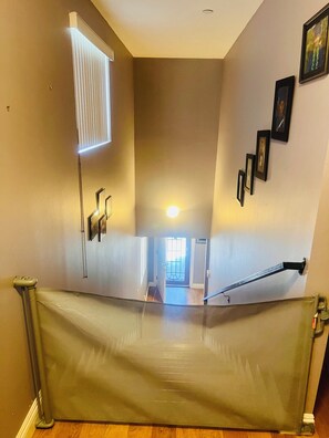 Eine Treppe mit Geländer, ein Fenster mit Jalousien und gerahmte Bilder an der Wand.