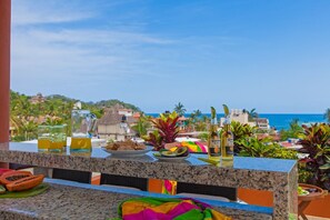 A balcony with a view of a coastal town, a plate of food, and two bottles of Corona Extra. - Beach Break Suites, 1 BR Suites Just Steps from Sayulita's Action (Sayulita)