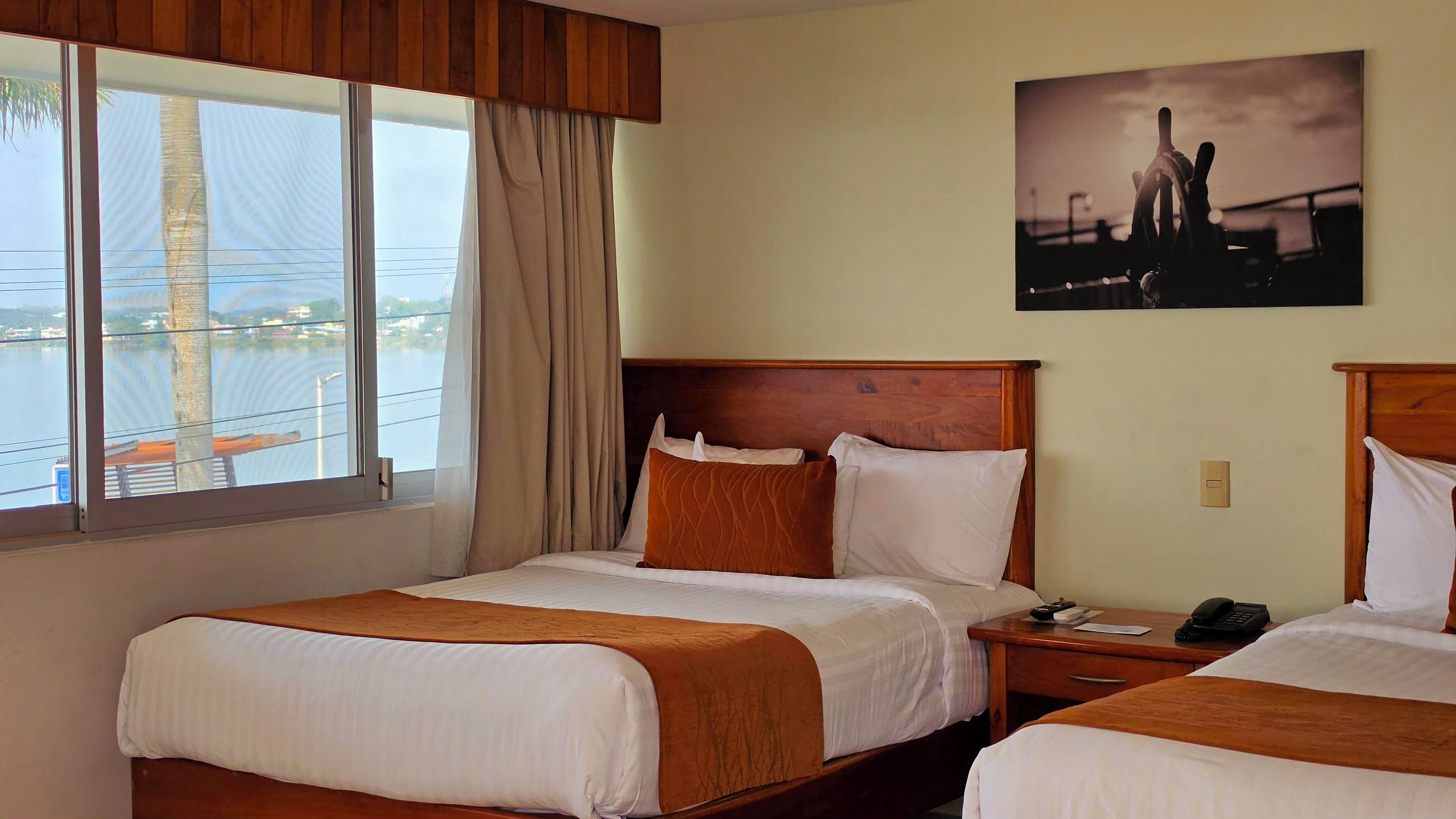 A hotel room with two beds, a view of a body of water, and a painting on the wall.
