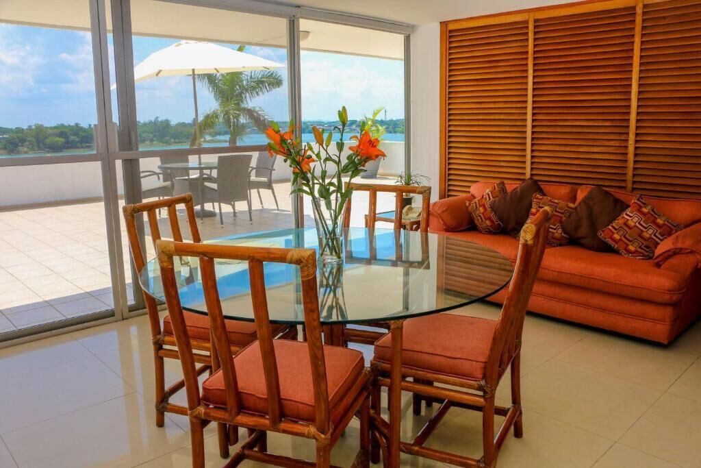 Een kamer met een glazen tafel, rieten stoelen, een bank met gestreepte kussens en uitzicht op de oceaan.