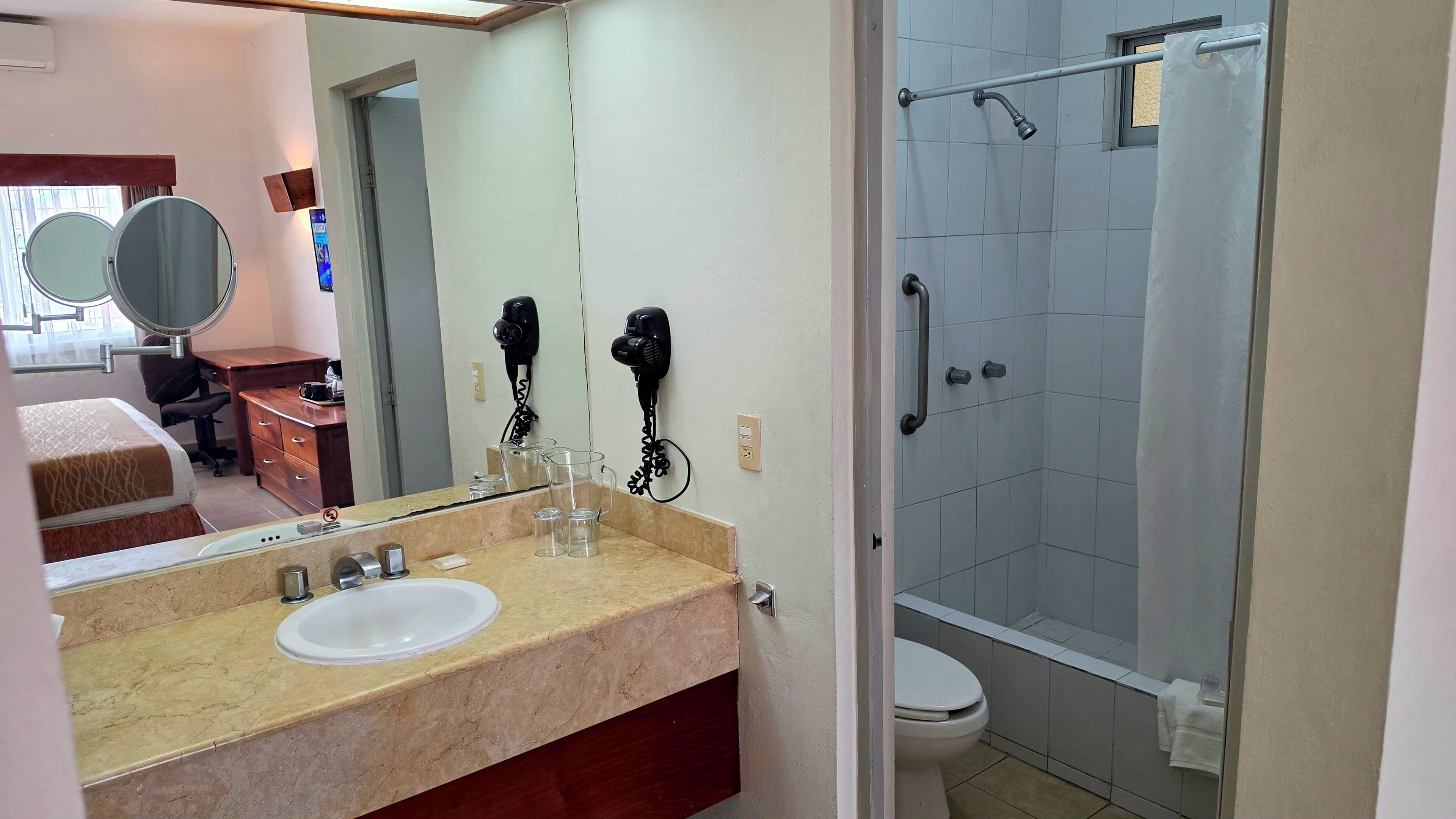 Une salle de bain équipée d’un lavabo, d’un miroir, d’un sèche-cheveux et d’une douche.