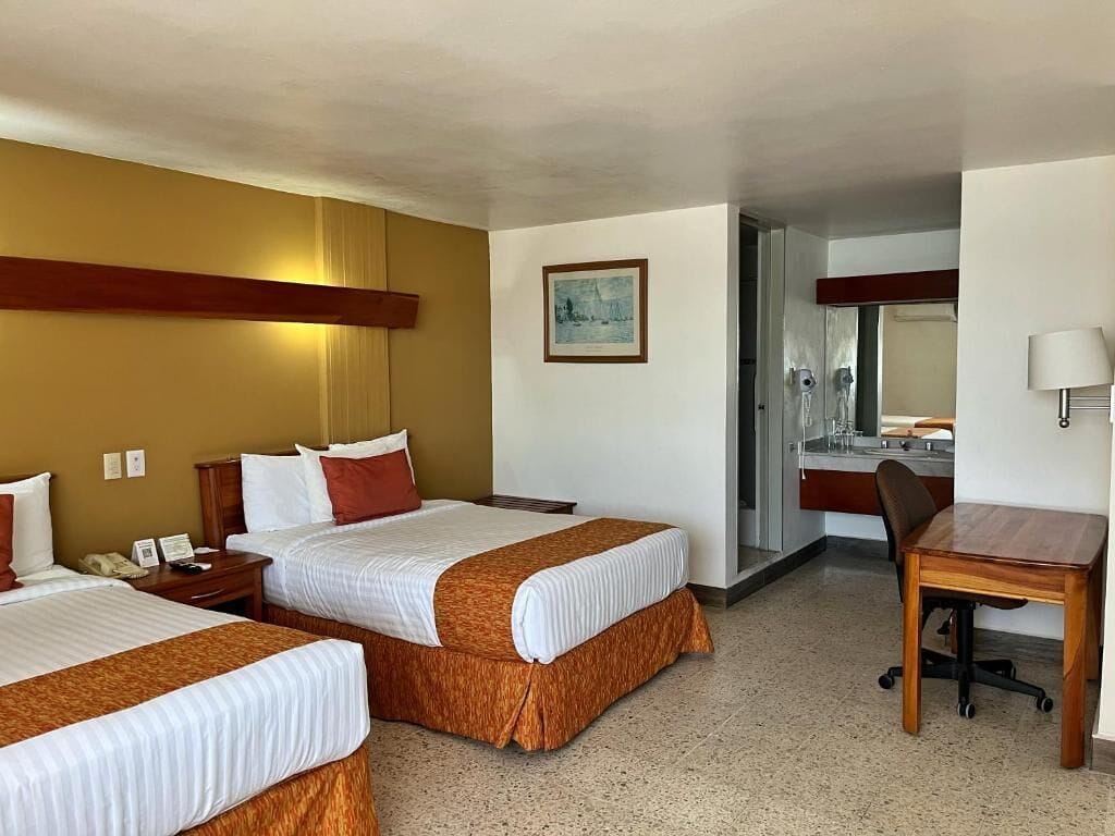 A hotel room with two beds, a desk, and a bathroom visible through an open door.