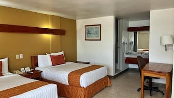 Habitación de hotel con dos camas, un escritorio y un baño visible a través de una puerta abierta.