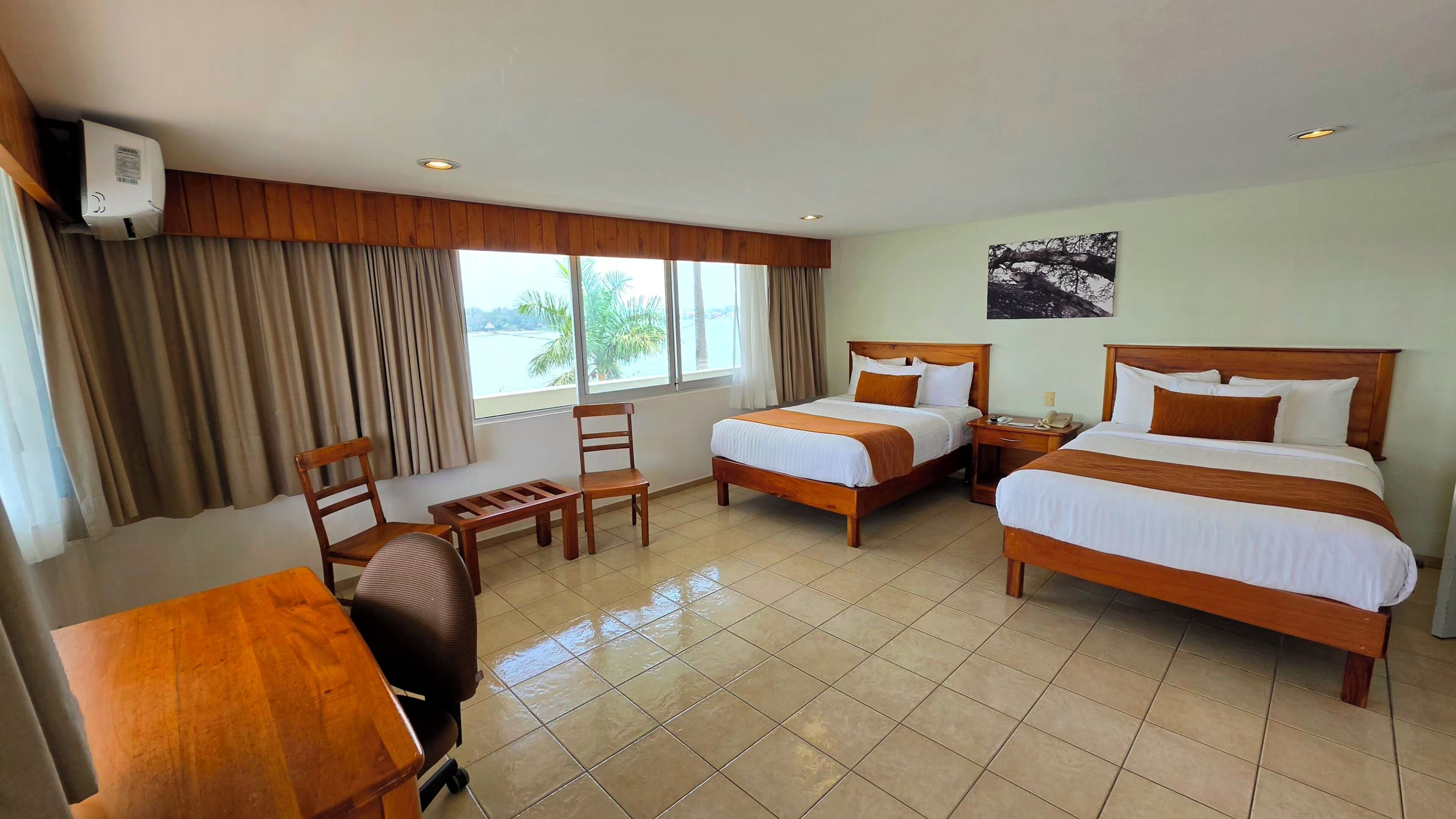 A hotel room with two beds, a desk, a chair, and a window with curtains.