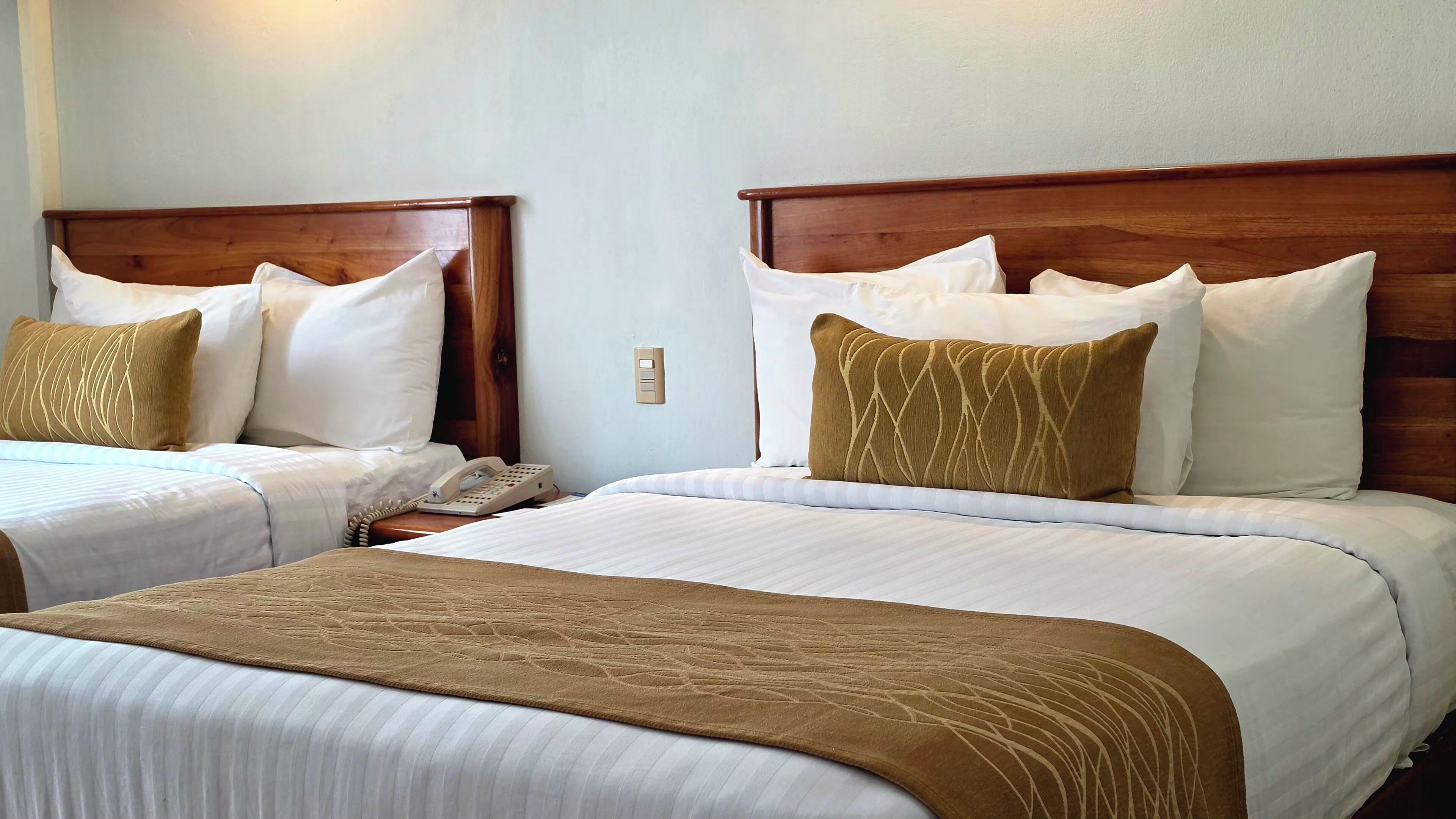 Two double beds with wooden headboards, white bedding, and brown decorative pillows.