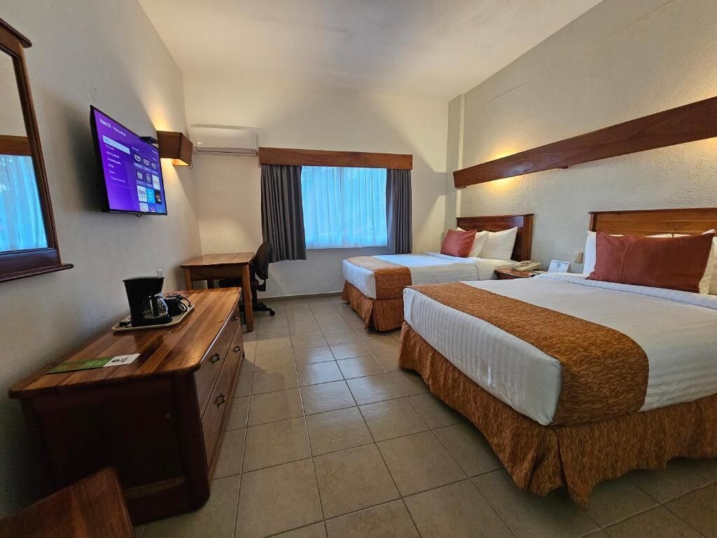 A hotel room with two beds, a desk, a chair, a TV, and a window with curtains.