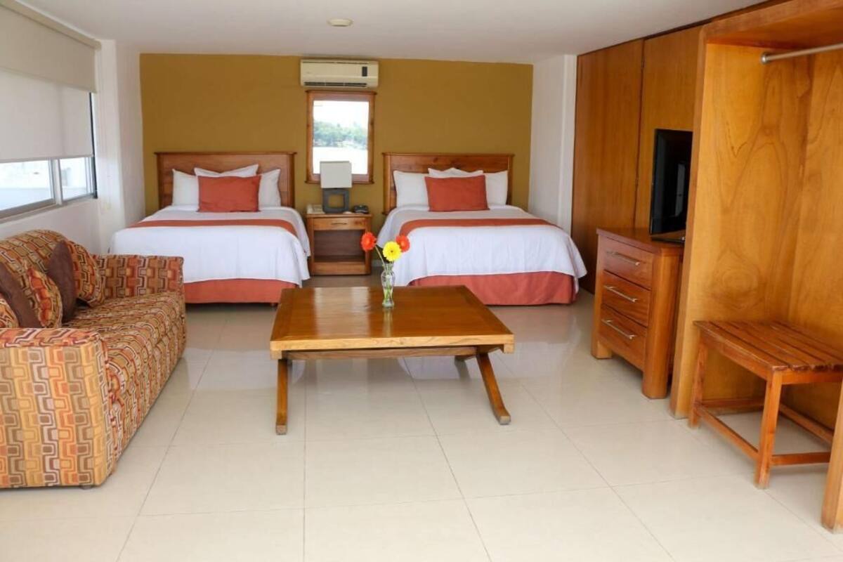 Una habitación de hotel con dos camas, un sofá, una mesa de madera, un televisor y un armario.