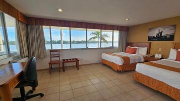 Habitación de hotel con dos camas, un escritorio, una silla y un ventanal con vistas al agua.