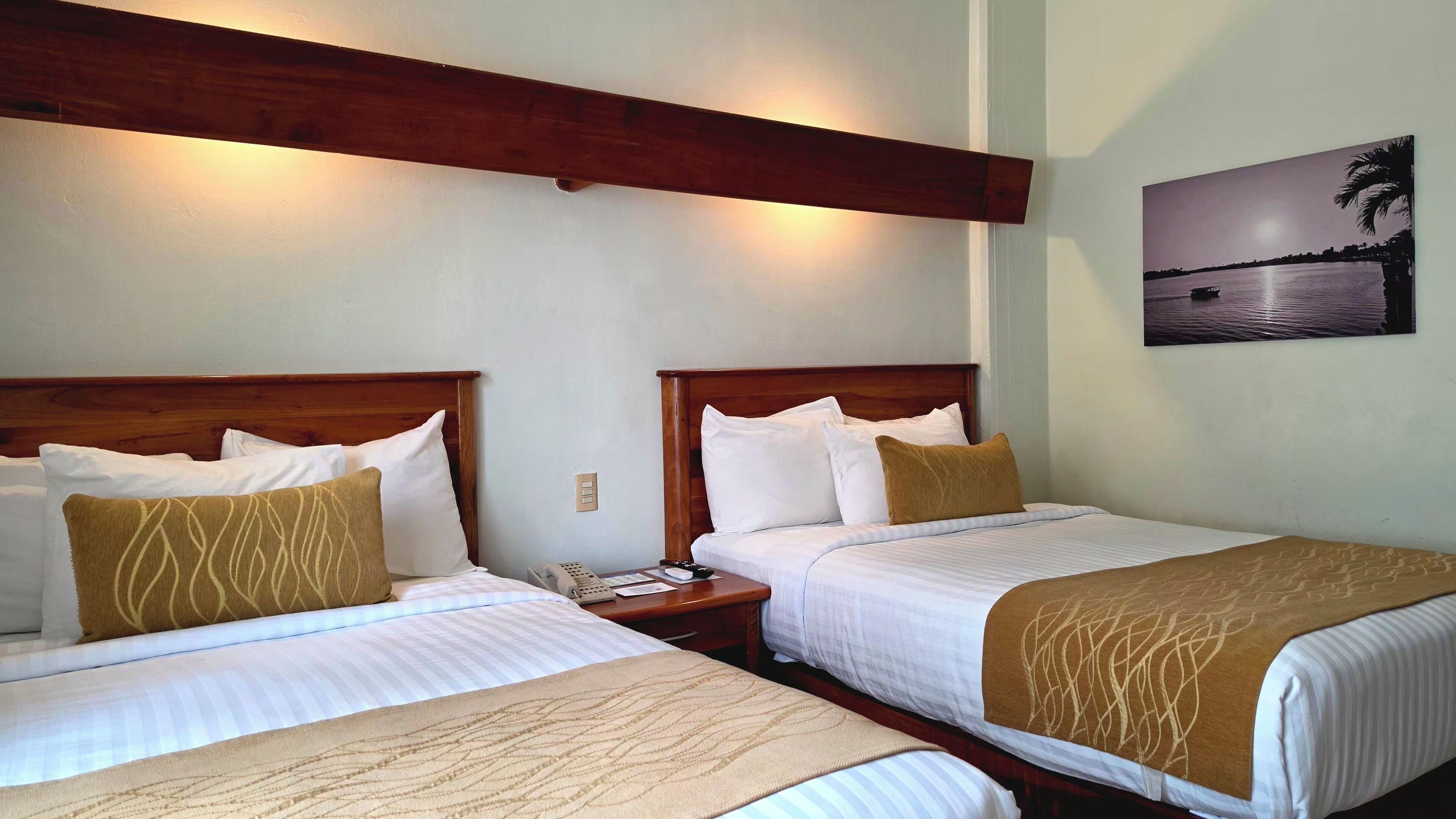 Two beds with wooden headboards, white bedding, and a nightstand with a phone and remote control.
