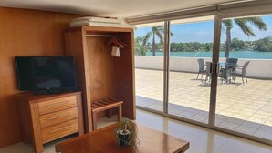 Una habitación con escritorio de madera, televisión, armario y balcón con mesa y sillas.