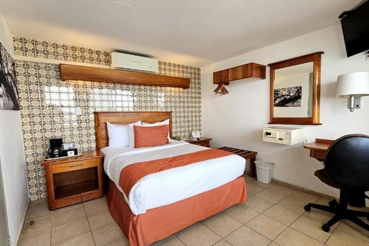 Habitación de hotel con cama, mesitas de noche, escritorio, silla, televisor, espejo y aire acondicionado instalado en la pared.