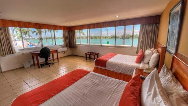 Habitación de hotel con dos camas, un escritorio y vista al mar.