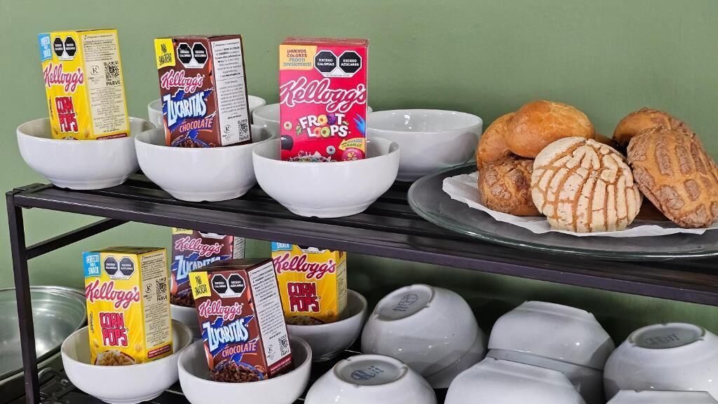 A shelf with bowls containing various Kellogg's cereal boxes and a plate with pastries.