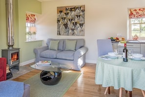 A living room with a sofa, a glass coffee table, a fireplace, a painting, and a dining area with a table set for two.