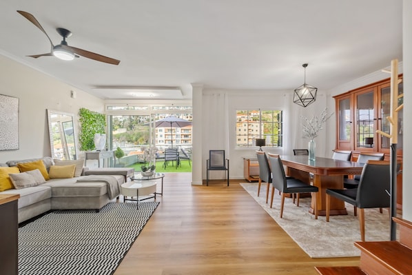 A modern living room with a sofa, dining table, and chairs, a ceiling fan, and large windows offering a view of the outside. - Villa Emilia by Atlantic Holiday (Calheta)