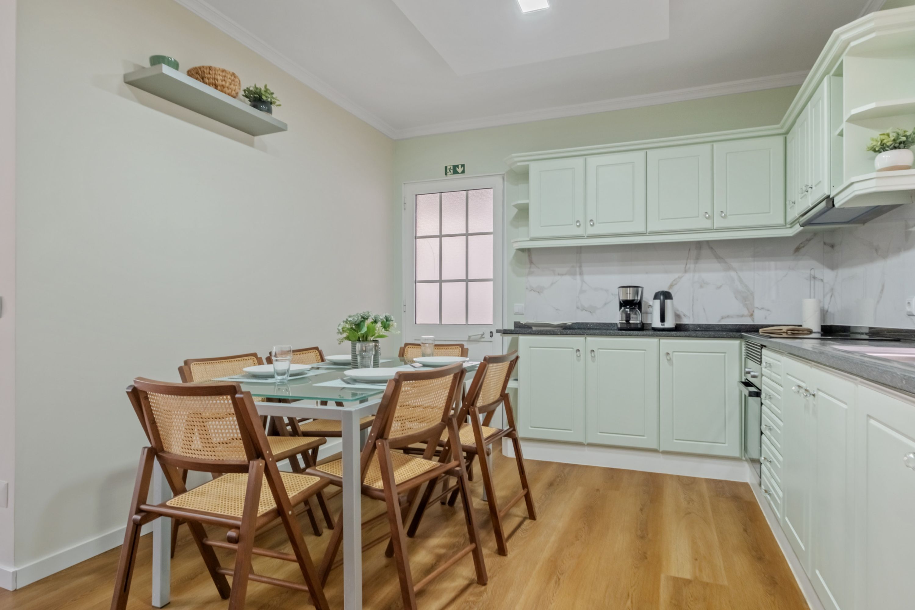 A modern kitchen with white cabinets, a marble backsplash, and a dining area with wicker chairs.