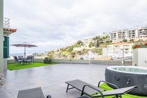 Eine Dachterrasse mit Whirlpool, Sitzgelegenheiten im Freien und Blick auf das Meer sowie Hügelhäuser.