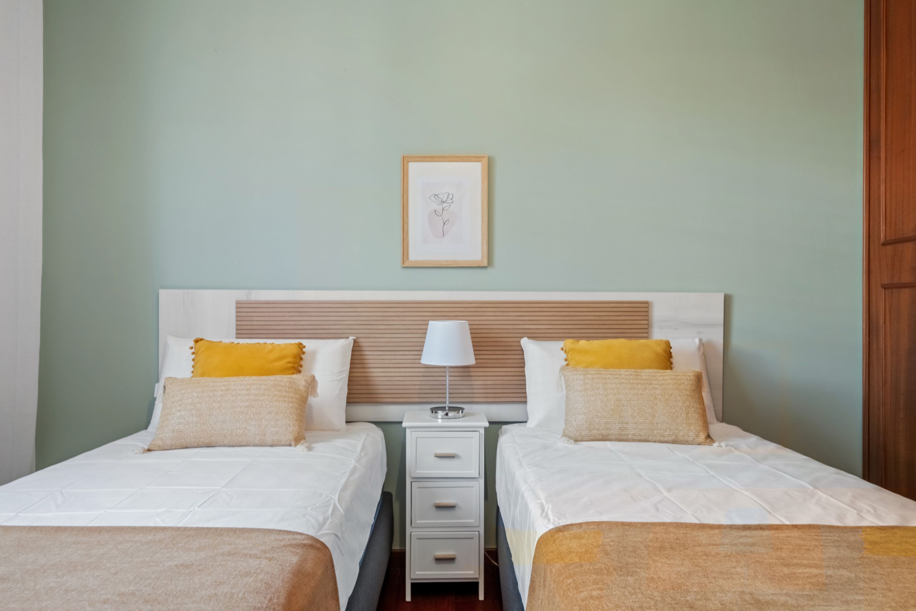 A double room with two beds, a nightstand with a lamp, and a framed picture on the wall.