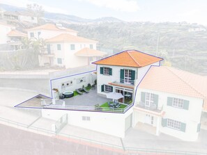 A two-story house with a tiled roof, a balcony, and a patio area with outdoor furniture. - Villa Emilia by Atlantic Holiday (Calheta)