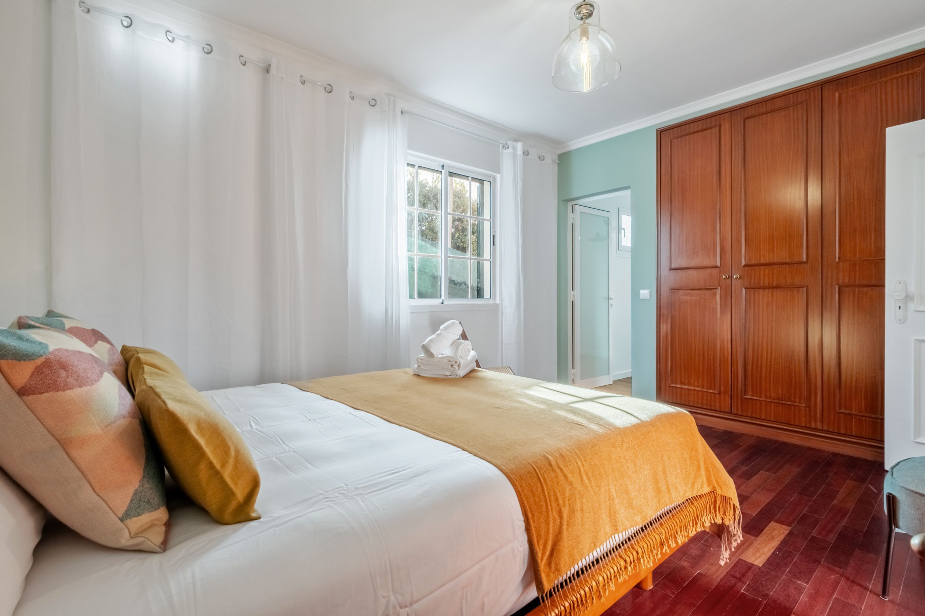 Un dormitorio con cama, cortinas, ventana, armario y puerta.