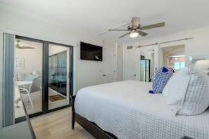 Ein Schlafzimmer mit Bett, Deckenventilator, an der Wand montiertem Fernseher und einer Glastür zum Balkon.