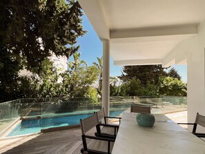 A poolside area with a glass railing, a table with chairs, and a view of a swimming pool. - Carthage Villa | 3BR Luxury · Pool · Garden (Carthage)