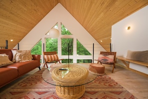 Ein modernes Loft mit schrägverdeckter Decke, großen Fenstern, einem Glastisch und einer gemütlichen Sitzecke.
