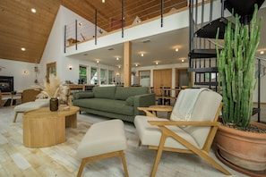 Ein geräumiger Innenraum mit einem grünen Sofa, Holzmöbeln, einer Kakteenpflanze und einer Wendeltreppe.