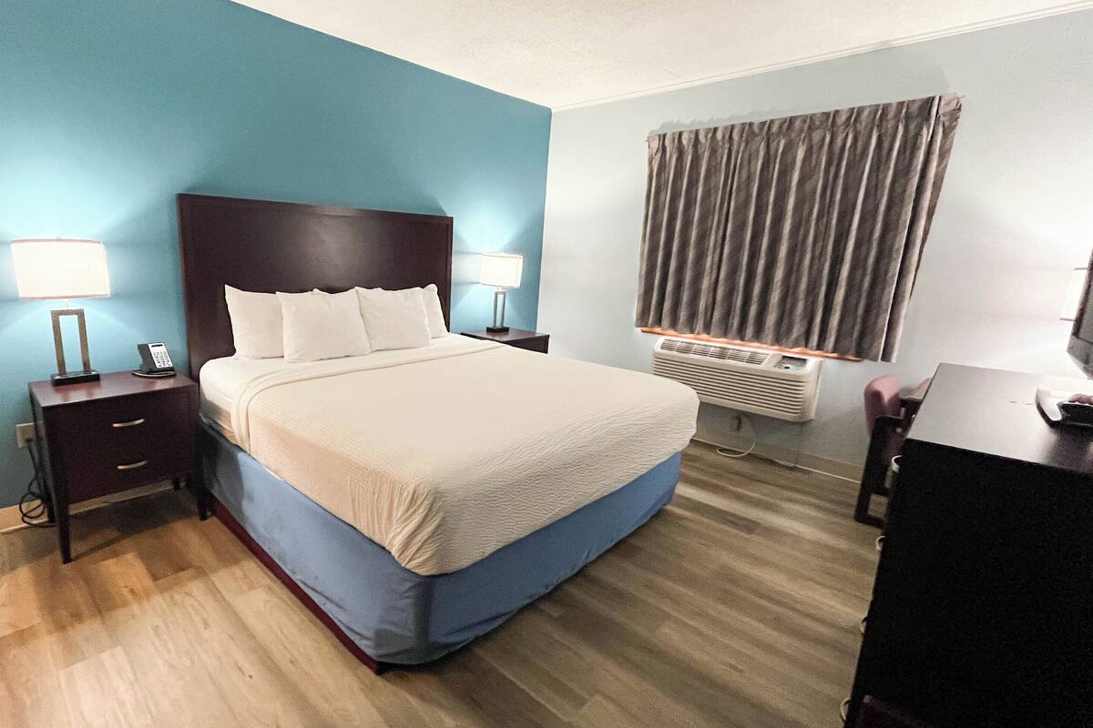 Quarto de hotel com cama, luminárias de cabeceira, escrivaninha e janela com cortinas.
