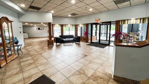 A spacious lobby with a reception desk, seating area, and a large window with a view of the outdoors. - Studio 6 Suites – Tiffin, Oh (Tiffin)