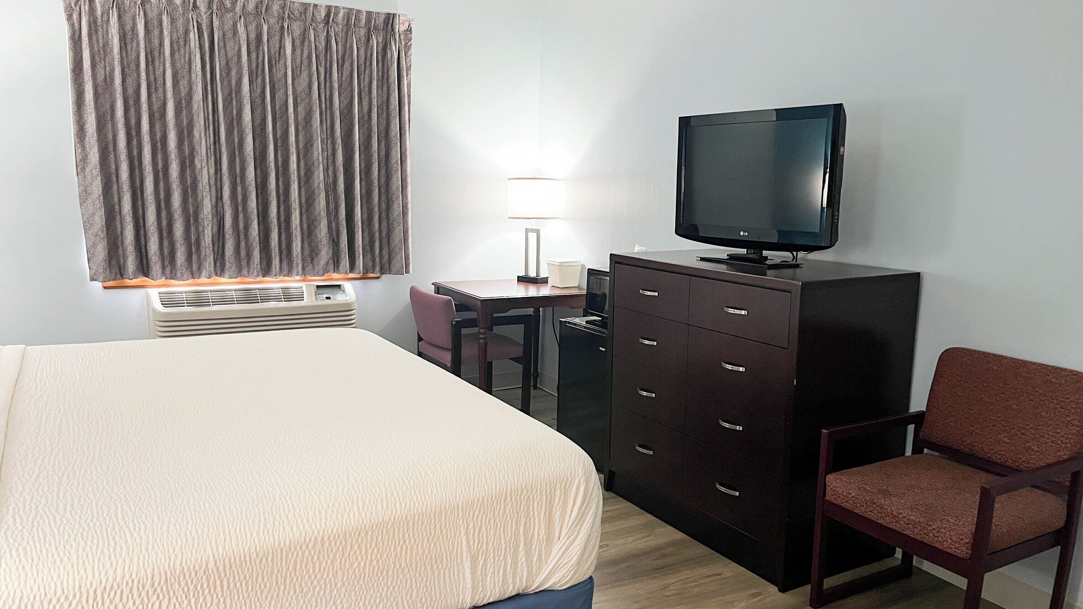 A hotel room with a bed, a desk, a television, a chair, a dresser, and a window with curtains.
