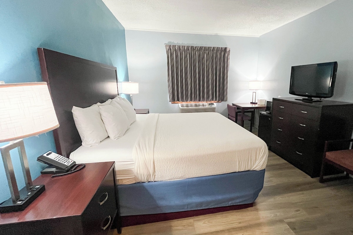 Quarto de hotel com cama, escrivaninha com telefone, televisão, cadeira e cômoda.