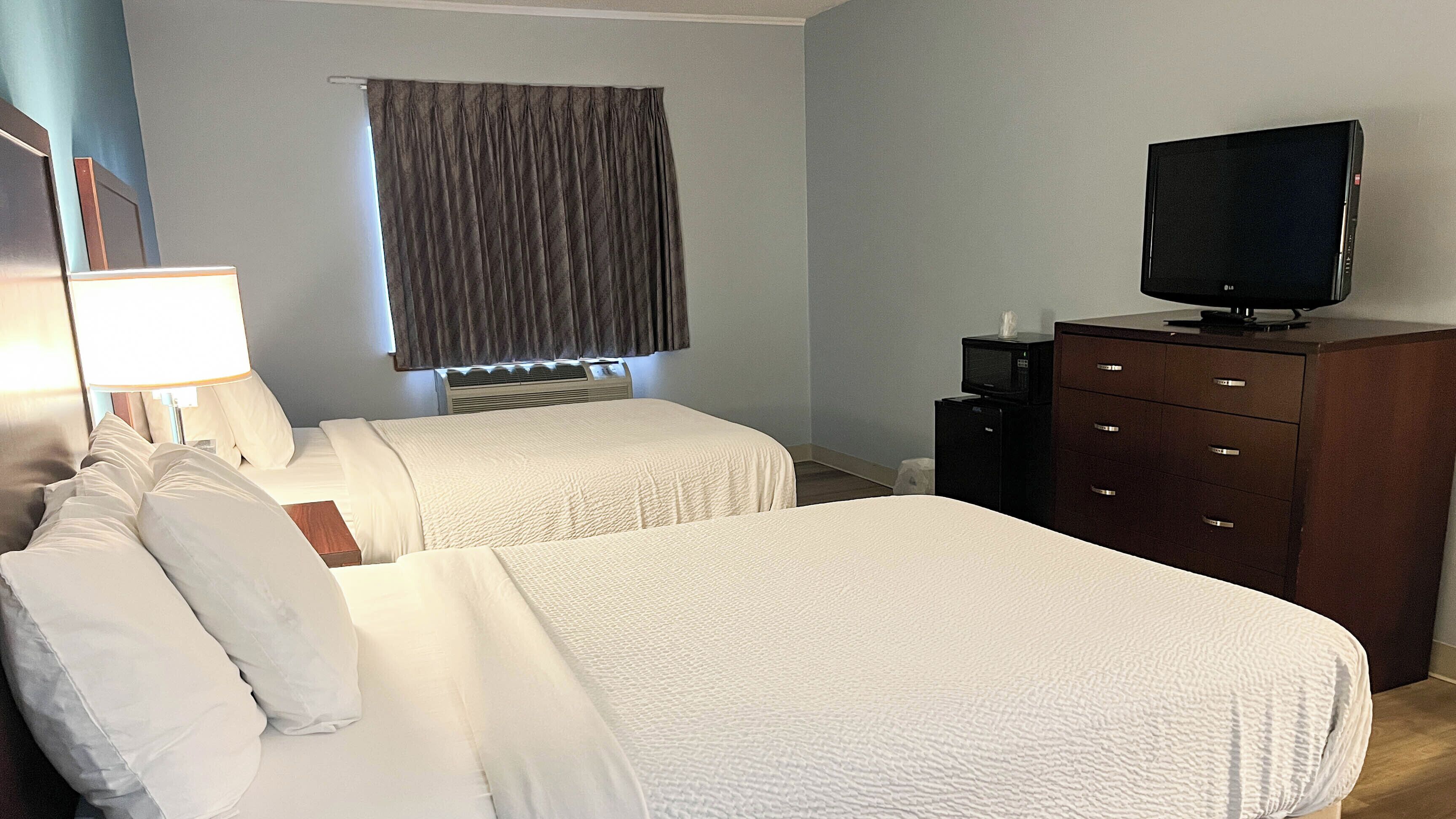 Habitación de hotel con dos camas, televisión, cómoda y ventana con cortinas.