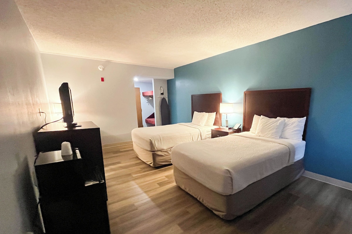 Quarto de hotel com duas camas, uma escrivaninha com computador e uma televisão.